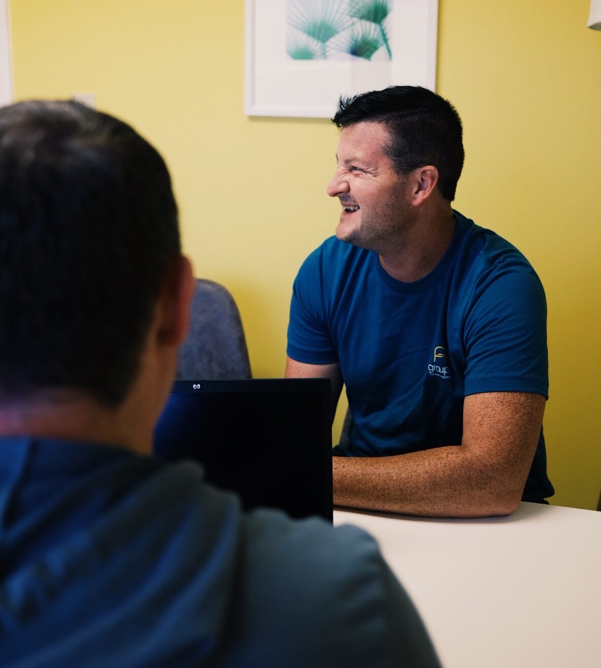 A male Groups member is sitting in a counselor's office smiling.